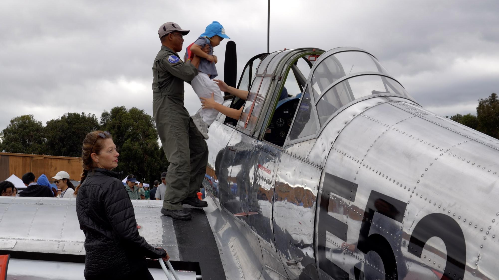 A pilot helps a child enter an old military plane at Palo Alto Airport Day